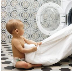 Baby sitting on floor in front of a washing machine pulling out laundry